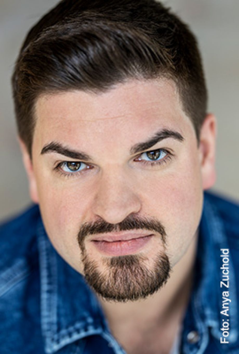 Das Bild zeigt Amber Chiara Eul, mit blondbraunen Haaren, die zu einem Dutt hochgesteckt sind. Sie hat blaue Augen und blickt mit ernstem Ausdruck direkt in die Kamera. Sie trägt einen rosafarbenen Pullover mit einem roten Streifen im Brustbereich. Der Hintergrund ist einfarbig rostbraun.