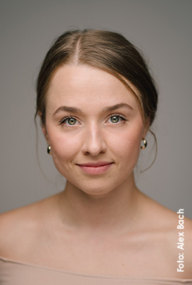 Das Portrait zeigt Jana Mayer mit zusammengebundenen braunen Haaren und hellen Augen. Sie blickt ruhig in die Kamera und lächelt dezent.