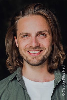 Das Portrait zeigt Robin Ziehbrunner mit schulterlangen, welligen, braunen Haaren und einem freundlichen Lächeln.