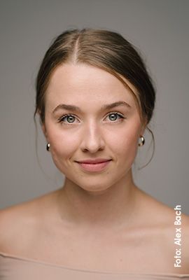 Das Portrait zeigt Jana Mayer mit zusammengebundenen braunen Haaren und hellen Augen. Sie blickt ruhig in die Kamera und lächelt dezent.