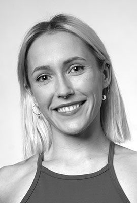 Das Bild zeigt Amber Chiara Eul, mit blondbraunen Haaren, die zu einem Dutt hochgesteckt sind. Sie hat blaue Augen und blickt mit ernstem Ausdruck direkt in die Kamera. Sie trägt einen rosafarbenen Pullover mit einem roten Streifen im Brustbereich. Der Hintergrund ist einfarbig rostbraun.