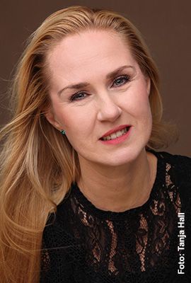 Das Portrait zeigt Jana Mayer mit zusammengebundenen braunen Haaren und hellen Augen. Sie blickt ruhig in die Kamera und lächelt dezent.