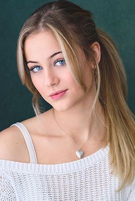 Das Portrait zeigt Shania Ochsner mit langen, zusammen gebunden blonden Haaren. Sie trägt ein weiß gesticktes Oberteil und eine dezente Halskette mit silbernem Herzanhänger.