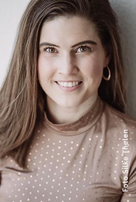 Das Portrait zeigt Steffi Regner mit langen, braunen Haaren und einem warmen Lächeln. Sie trägt ein beigefarbenes Oberteil mit glänzenden Punkten und goldene Ohrringe.